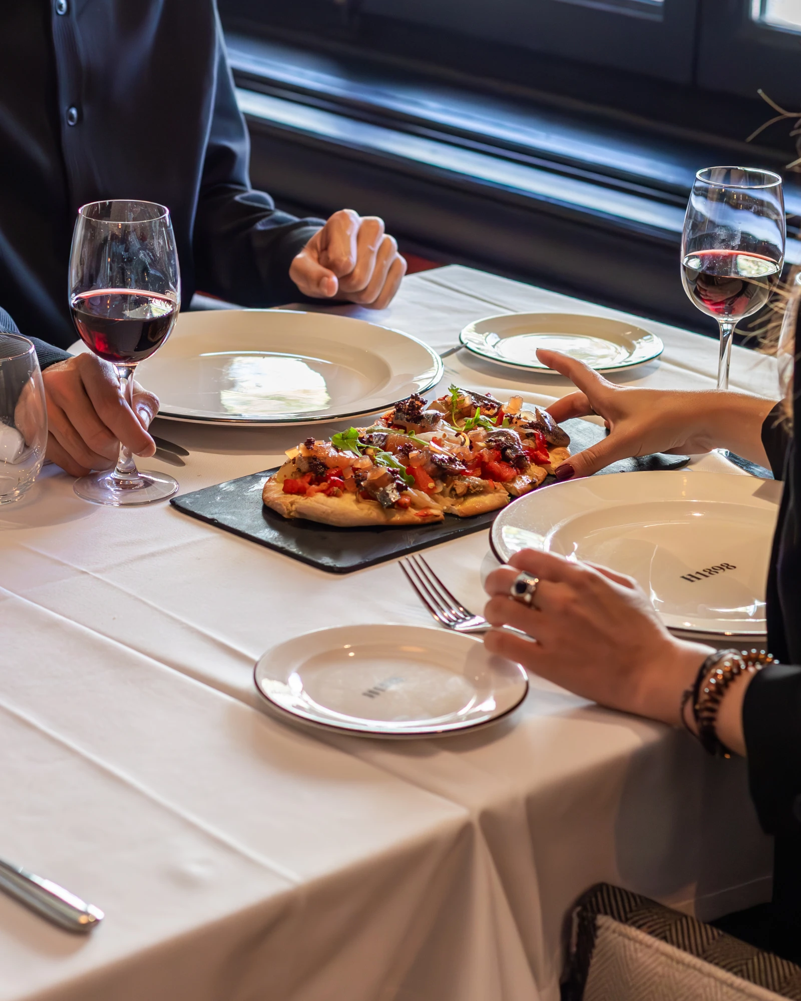 Mehrere Personen essen an einem Tisch mit Tellern, Pizza und Weingläsern.