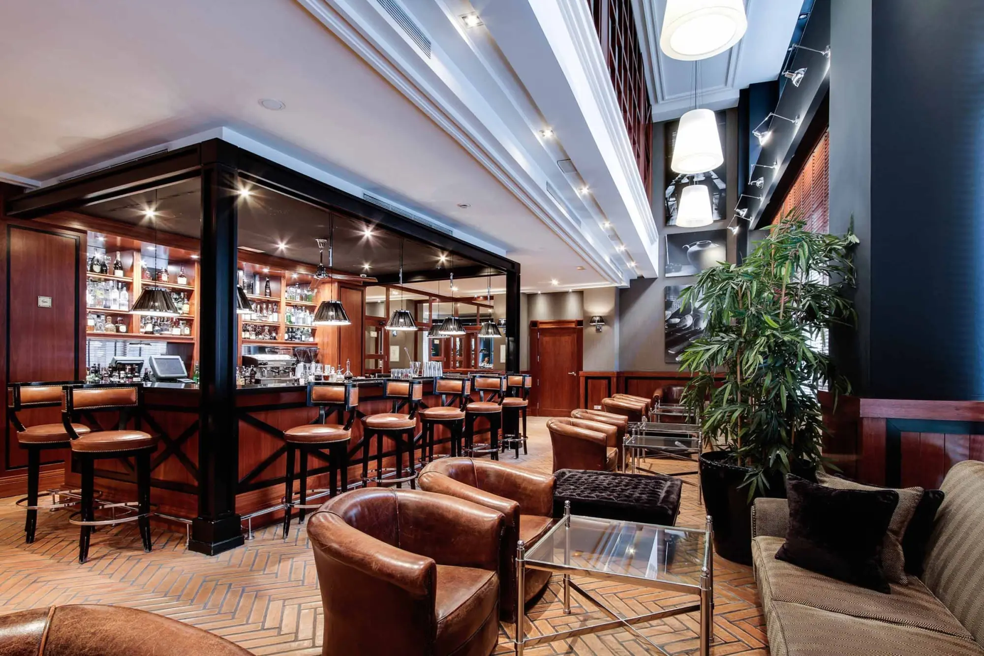 Se ve un bar interior con mesas, sillas y estanterías con botellas, junto a una zona de asientos.