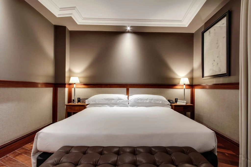 Si vede un letto matrimoniale con testiera imbottita e due comodini in una stanza con pareti beige.