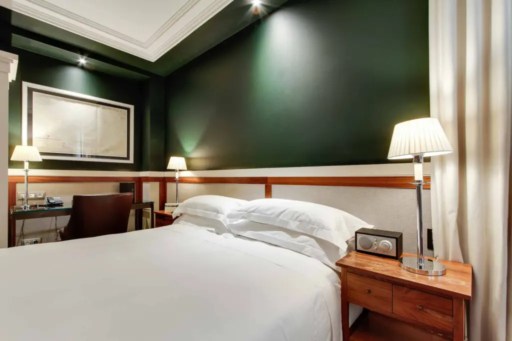 Es veu un llit doble amb capçal encoixinat i dues tauletes de nit en una habitació amb parets verdes.