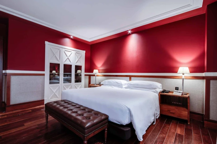Describe una habitación con cama doble, mesitas de noche y paredes rojas iluminadas.
