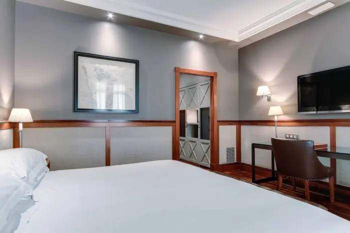 La imagen muestra una cama doble, dos lámparas de mesilla y un televisor en una habitación moderna.