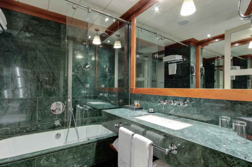 Se ve un baño moderno con ducha de vidrio, lavabo doble y grifería cromada.