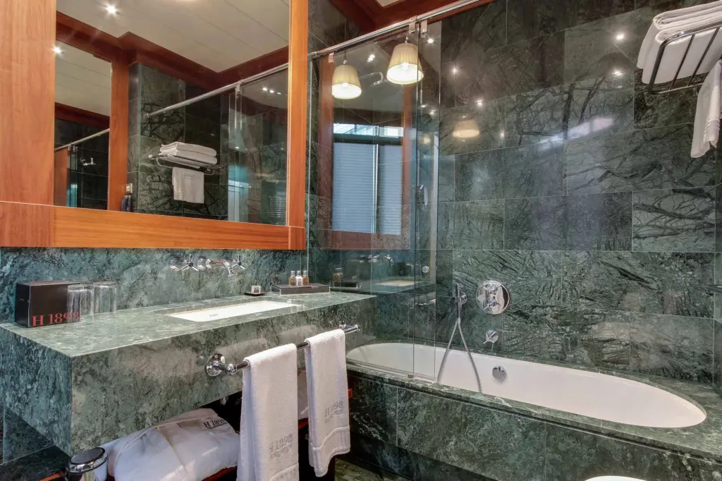 Se ve una bañera ovalada, una ducha de vidrio y un lavabo en un baño con paredes de piedra.