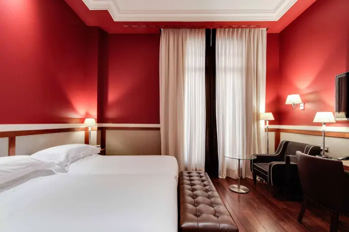 Im Zimmer sind ein Doppelbett, Vorhänge und ein Sitzbereich mit Sessel und Beistelltisch zu sehen.