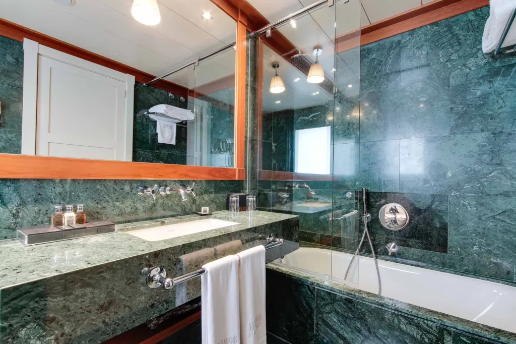 Das Badezimmer verfügt über eine Badewanne, ein Doppelwaschbecken mit Steinplatte und eine Dusche mit Glasabtrennung.