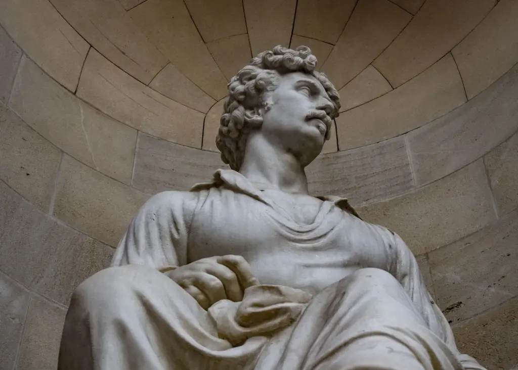 Estatua de mármol de un hombre con túnica, apoyado en una mano, sobre un fondo de pared curva.