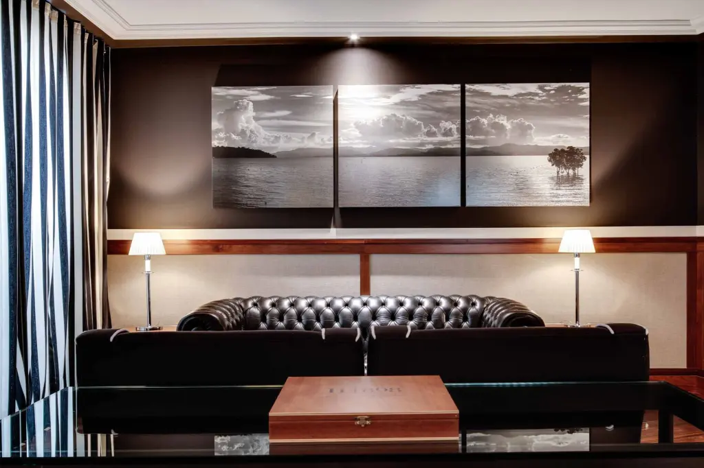 On voit un canapé-lit avec une tête de lit rembourrée, deux lampes et un tableau panoramique sur le mur.