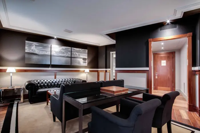 L'image montre un salon avec un canapé, des fauteuils, une table et un mur avec des tableaux.