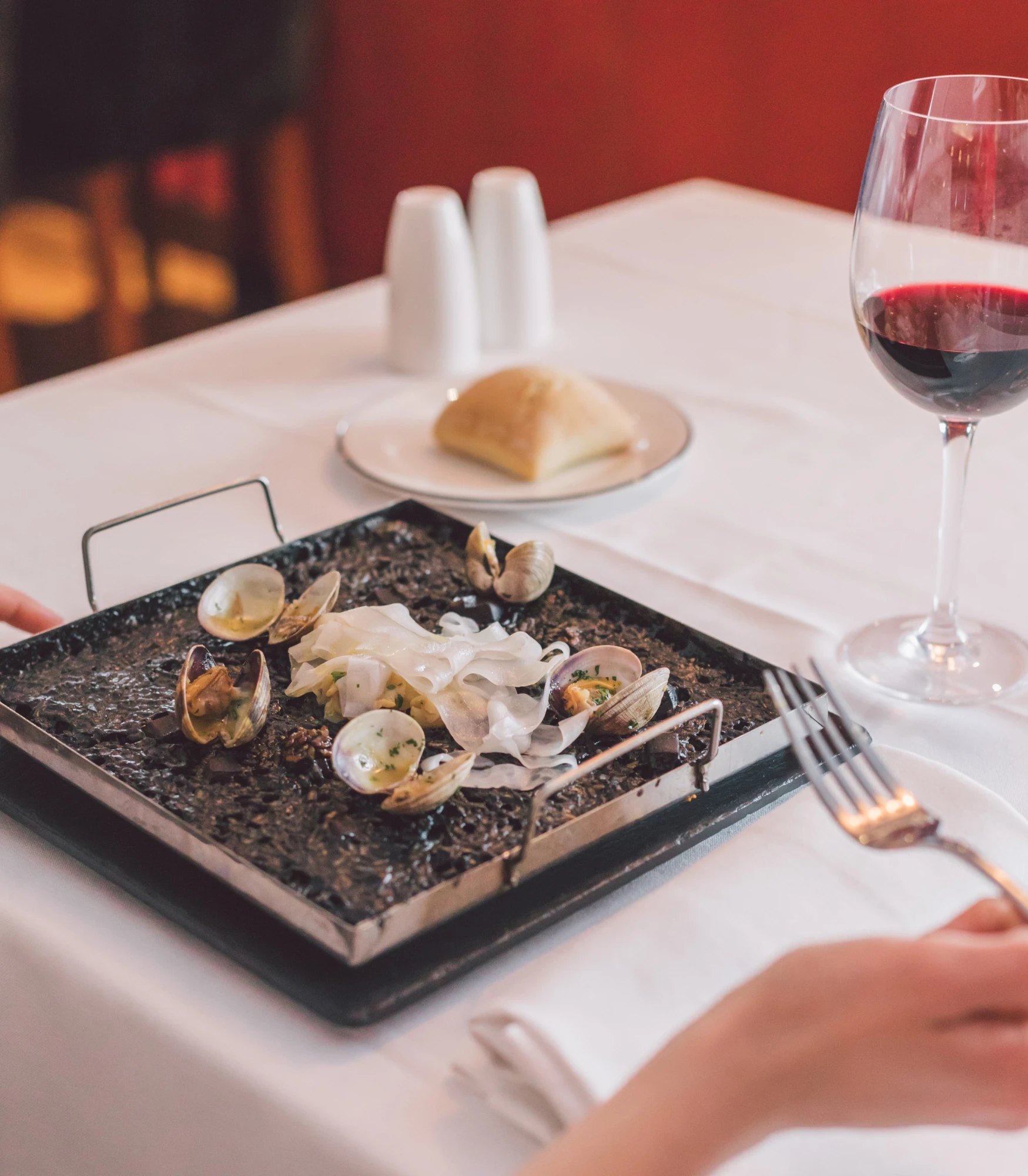 Una mesa con una plancha de mariscos, pan y dos copas de vino sobre un mantel blanco.