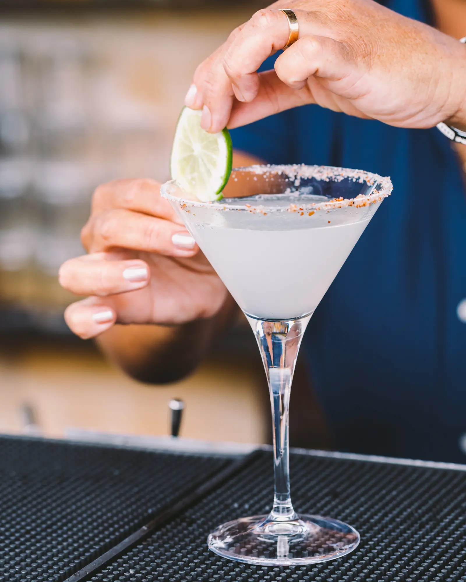 Une personne tient un verre de cocktail avec une tranche de citron vert sur la table.