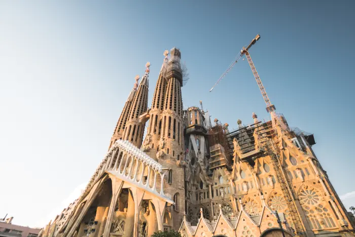 La basilica della Sagrada Familia è visibile con impalcature e gru contro il cielo azzurro.