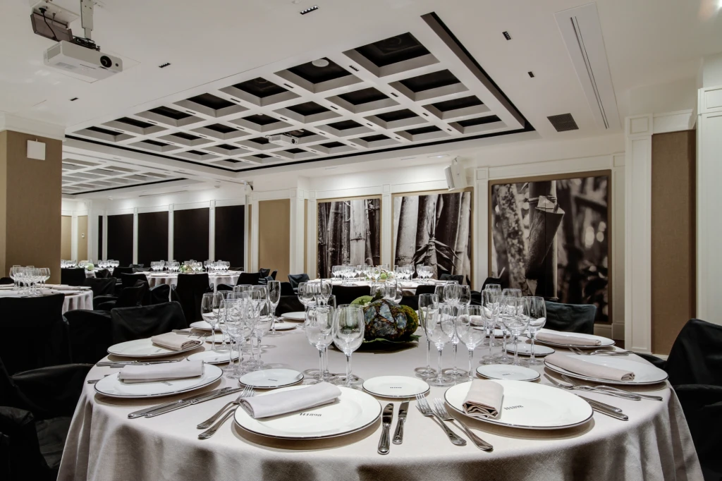 There is a table set with tableware and glasses in a dining room with decorated walls and chairs around it.