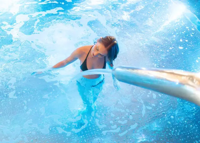 Una mujer nada en una piscina con agua azul y burbujas visibles.