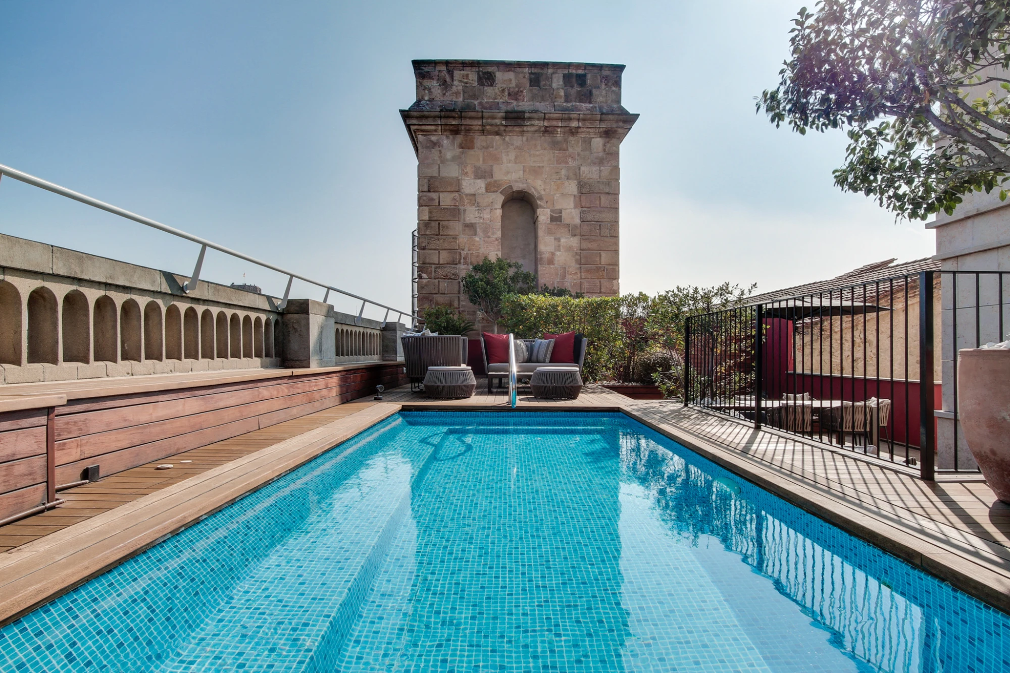 Man sieht einen rechteckigen Pool mit Holzrand und eine Terrasse mit Liegen und Geländern.
