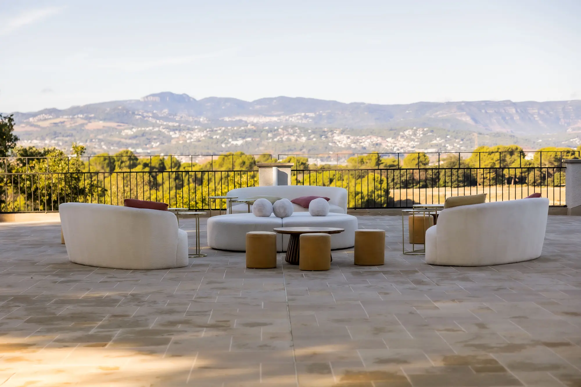 La terraza muestra sillones blancos, una mesa baja y cojines, con barandilla y montañas al fondo.