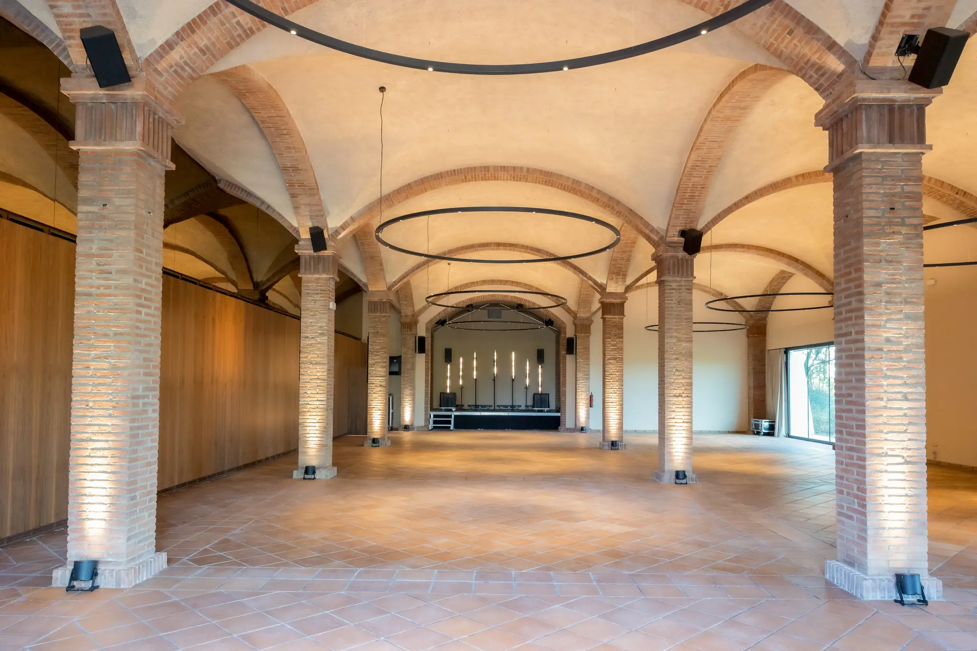 El pasillo interior muestra arcos de ladrillo, columnas y suelo de piedra bajo lámparas colgantes.