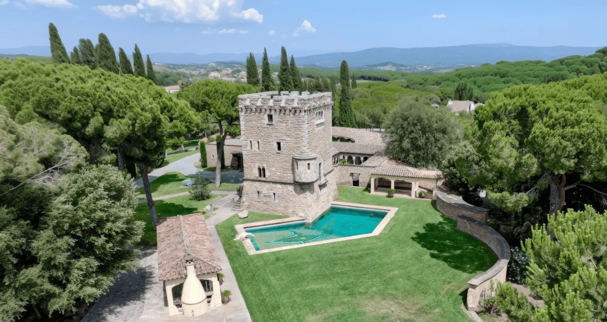 Se ve una villa de piedra con piscina y jardín, rodeada de vegetación y caminos exteriores.