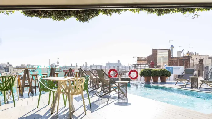 Se ve una terraza con sillas y una piscina al aire libre junto a una vista urbana.