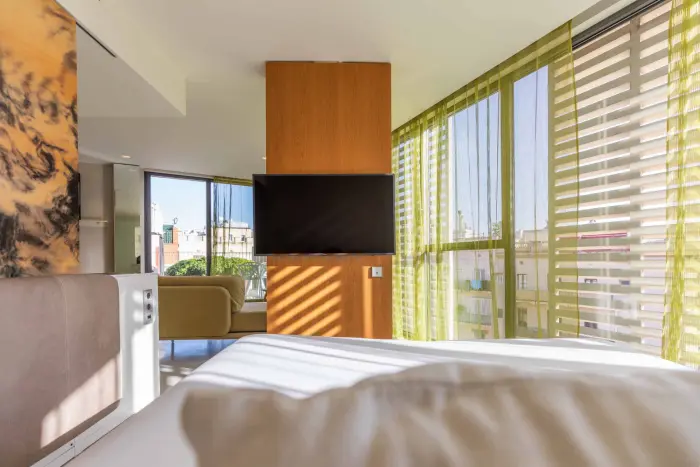 Se ve una cama con ropa de cama blanca y una ventana con cortinas a rayas verdes y beige.