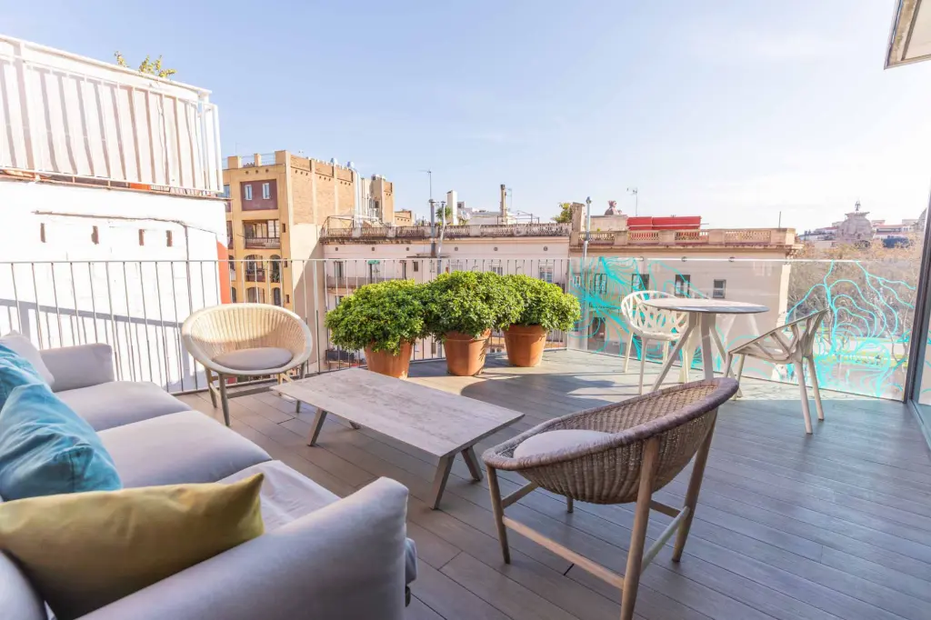 La terraza tiene un sofá, una mesa de madera y sillas de mimbre junto a macetas y una zona de estar al aire libre.