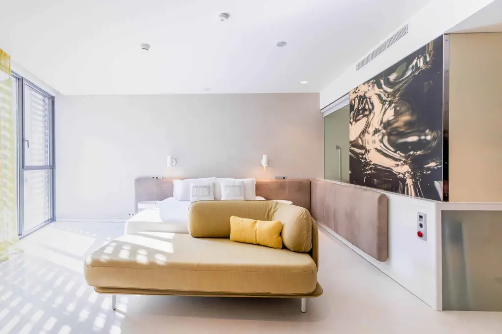 El dormitorio muestra una cama con cojines, una ventana y una pared con cuadros.
