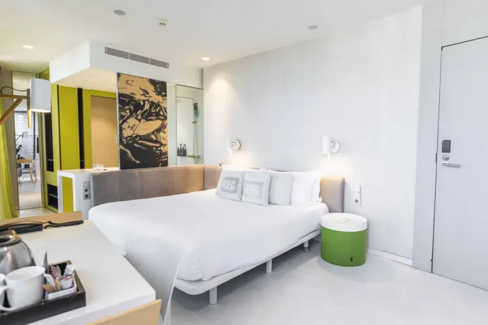 Se ve una habitación con una cama doble, mesitas y lámparas junto a una pared blanca.