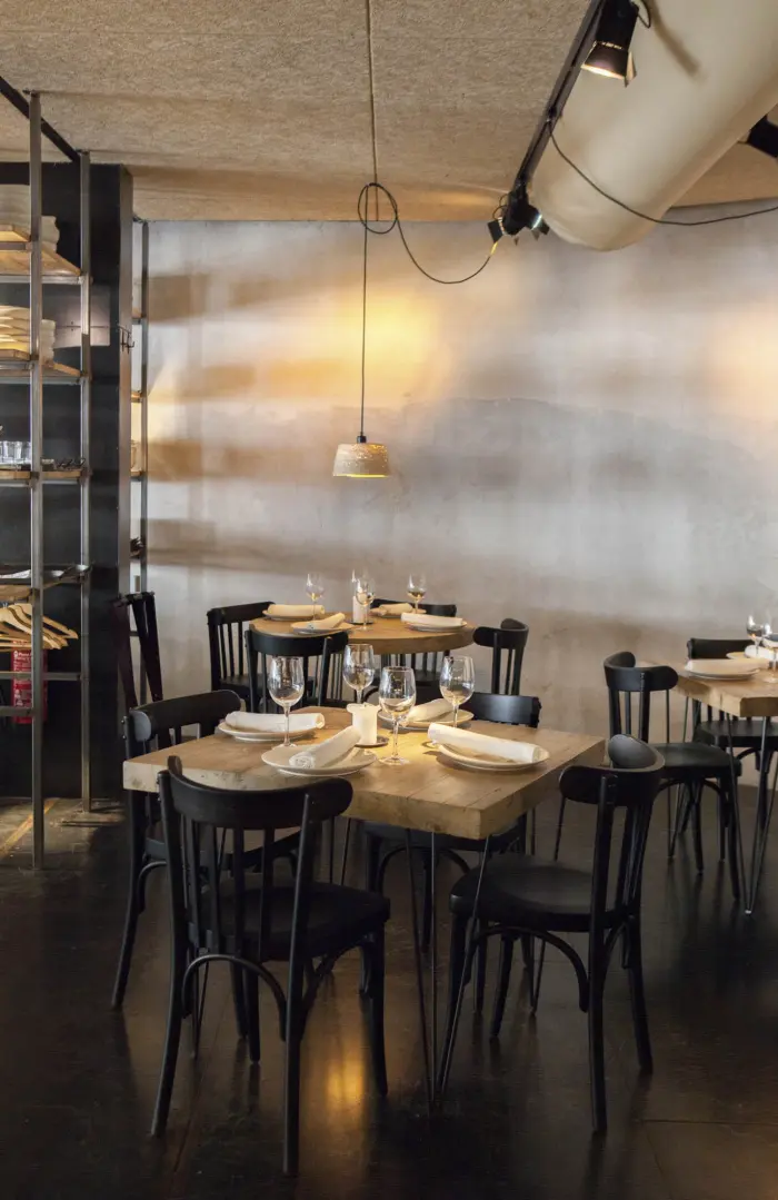 Se ve un comedor con mesas de madera, sillas negras y lámparas colgantes sobre la pared.