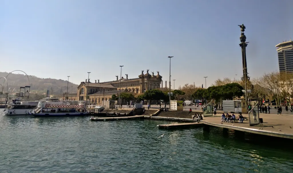 Se ve un paseo marítimo con muelle, barcos y edificios junto al agua.