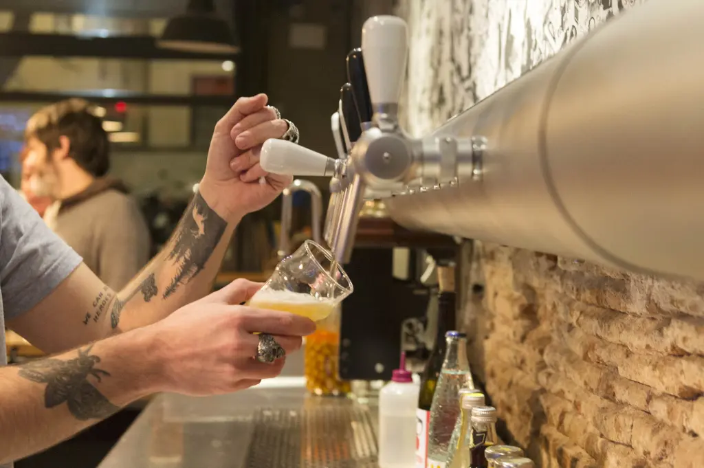 Una persona sirve cerveza desde un grifo sobre una barra con vasos y botellas.
