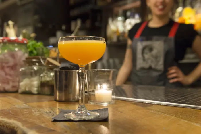 Sirven un cóctel naranja en una barra con una camarera detrás.