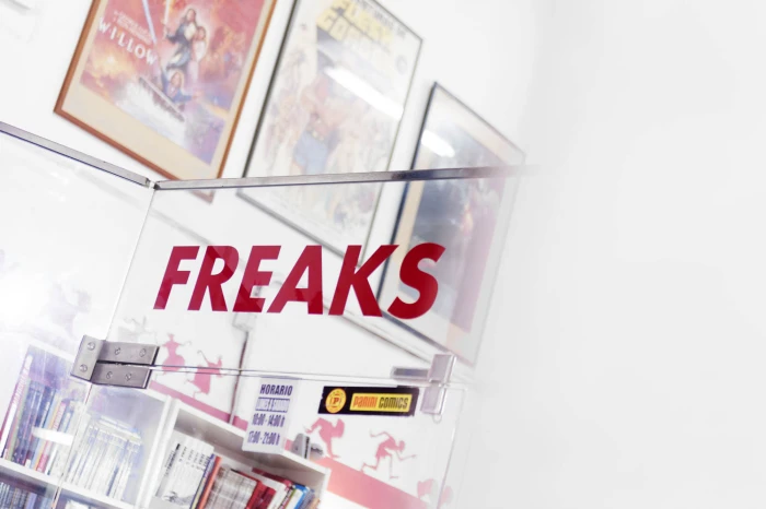 Se ve un cartel rojo con la palabra “FREAKS” dentro de una vitrina con pósters y folletos alrededor.