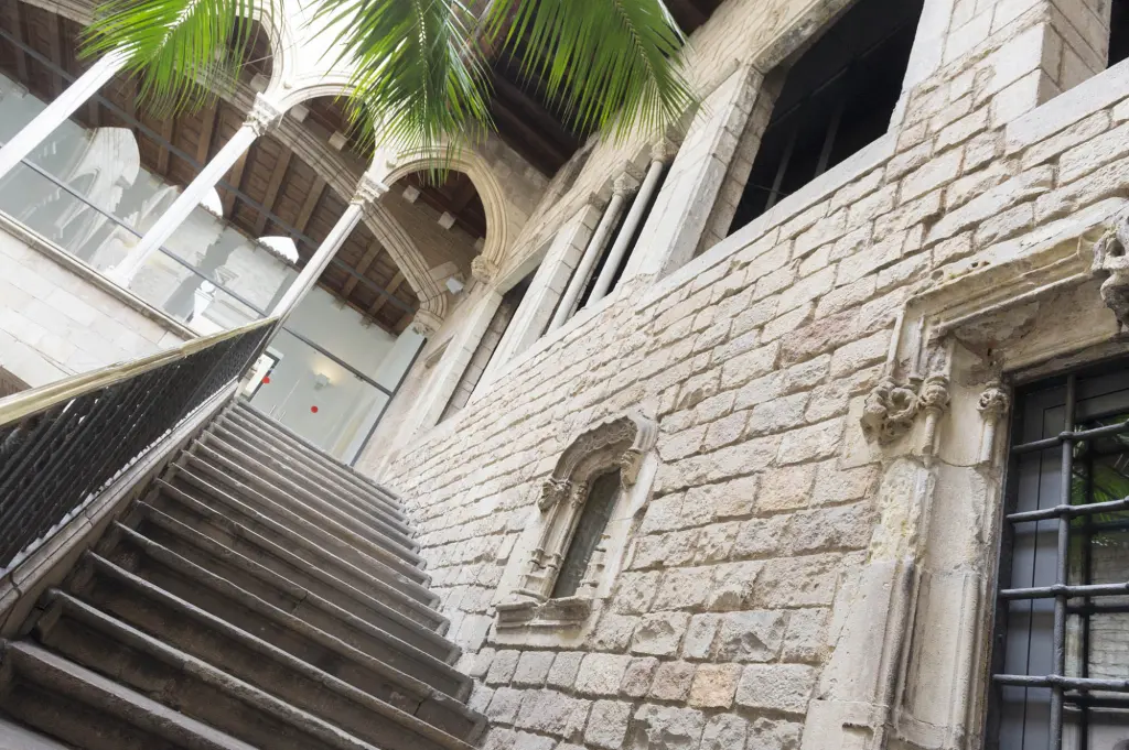Se ve un patio interior con escaleras, muros de piedra y una ventana con rejas.