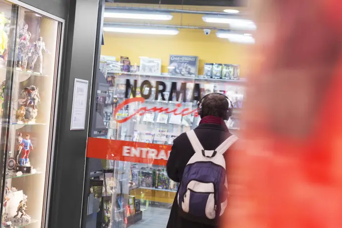 Una persona con mochila entra a una tienda con el letrero “NORMA” y “ENTRADA”.