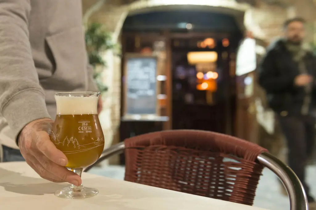 Sirve una copa con bebida sobre una mesa junto a una silla de mimbre en un entorno interior.