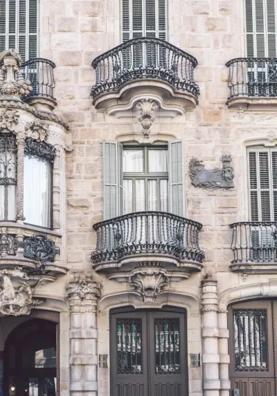 Se ve una fachada de piedra con balcones de hierro y ventanas con marcos decorativos.
