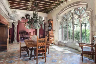 Se ve un salón amplio con mesas de madera, sillas, suelo de mosaico y grandes ventanales arqueados con luz natural.