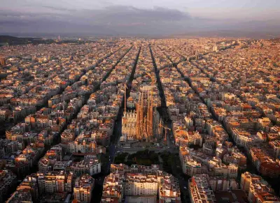 Es veu un paisatge urbà de l’Eixample amb carrers llargs i edificis densos sota un cel ennuvolat.