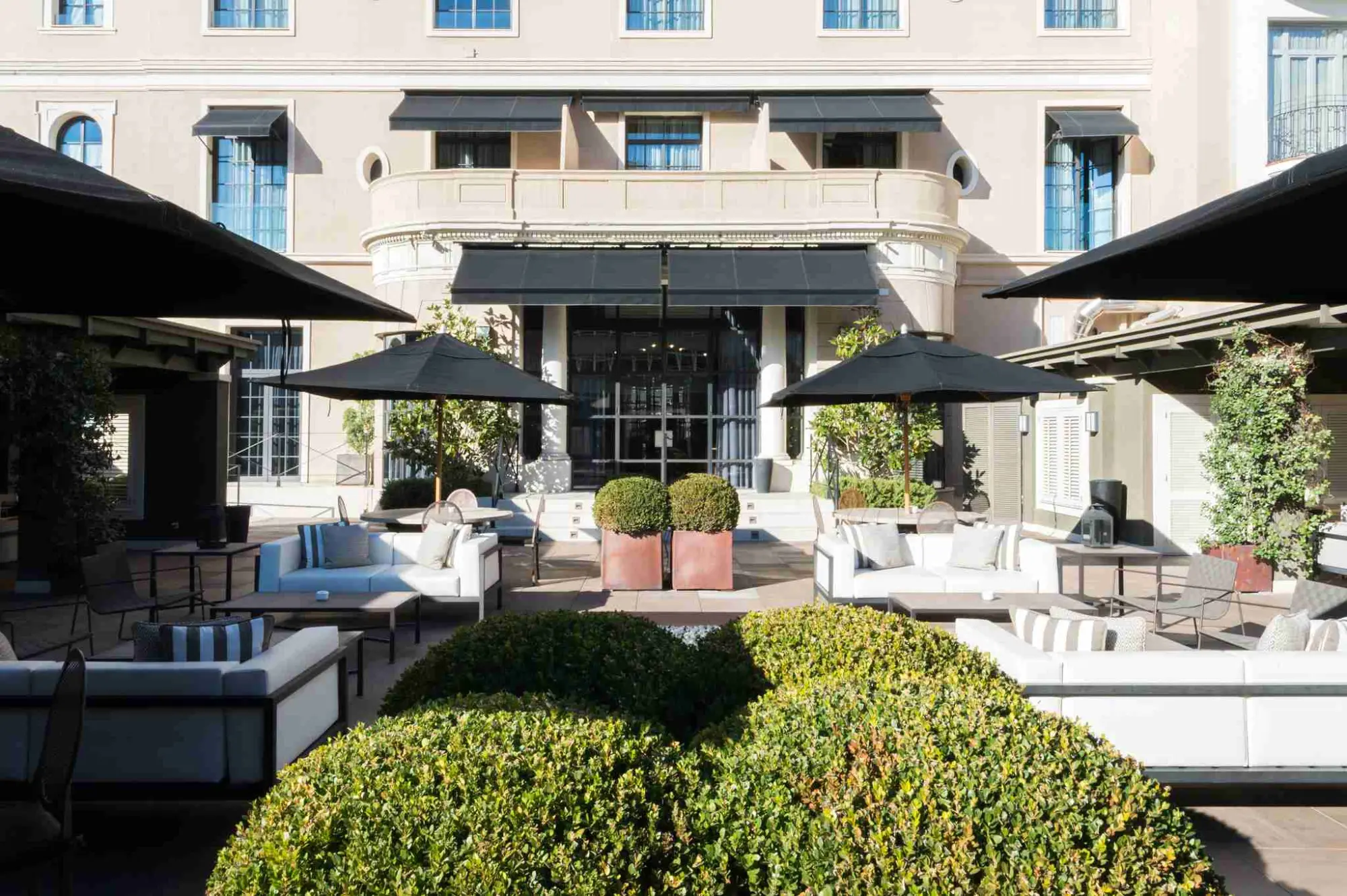 Si vede un cortile interno con divani, lettini e fioriere accanto a una zona coperta.