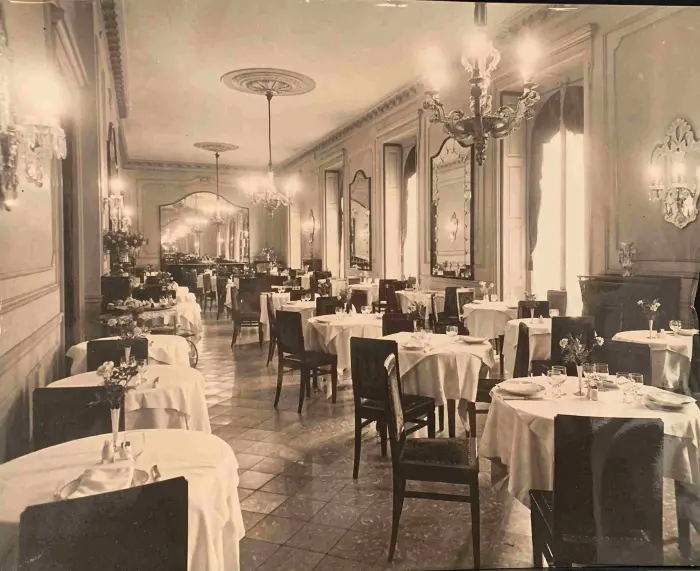 Se ve un comedor con mesas cubiertas y sillas alrededor, con lámparas colgantes y paredes decoradas.