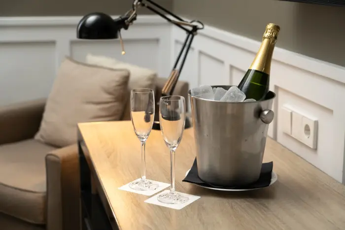 Se ve una mesa con una cubitera metálica con botellas y dos copas sobre un sofá tapizado.