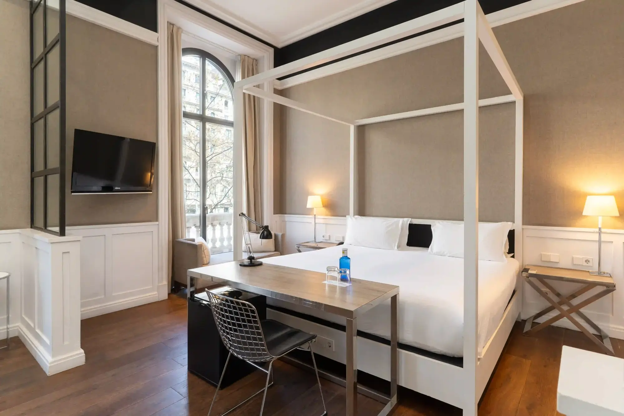 Se ve una habitación con cama, escritorio, sofá y una ventana con luz natural.