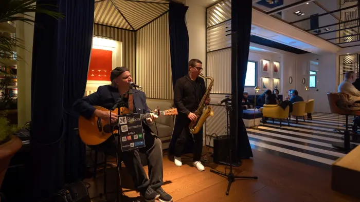 Se ve un escenario con músicos y equipo de sonido en una sala con asientos y luces decorativas.