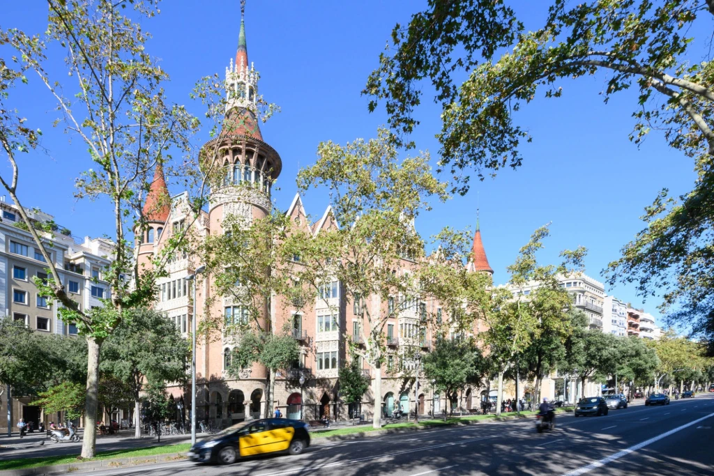 Es veu una torre modernista de maó i ceràmica amb cúpula, envoltada d'arbres sota un cel blau.