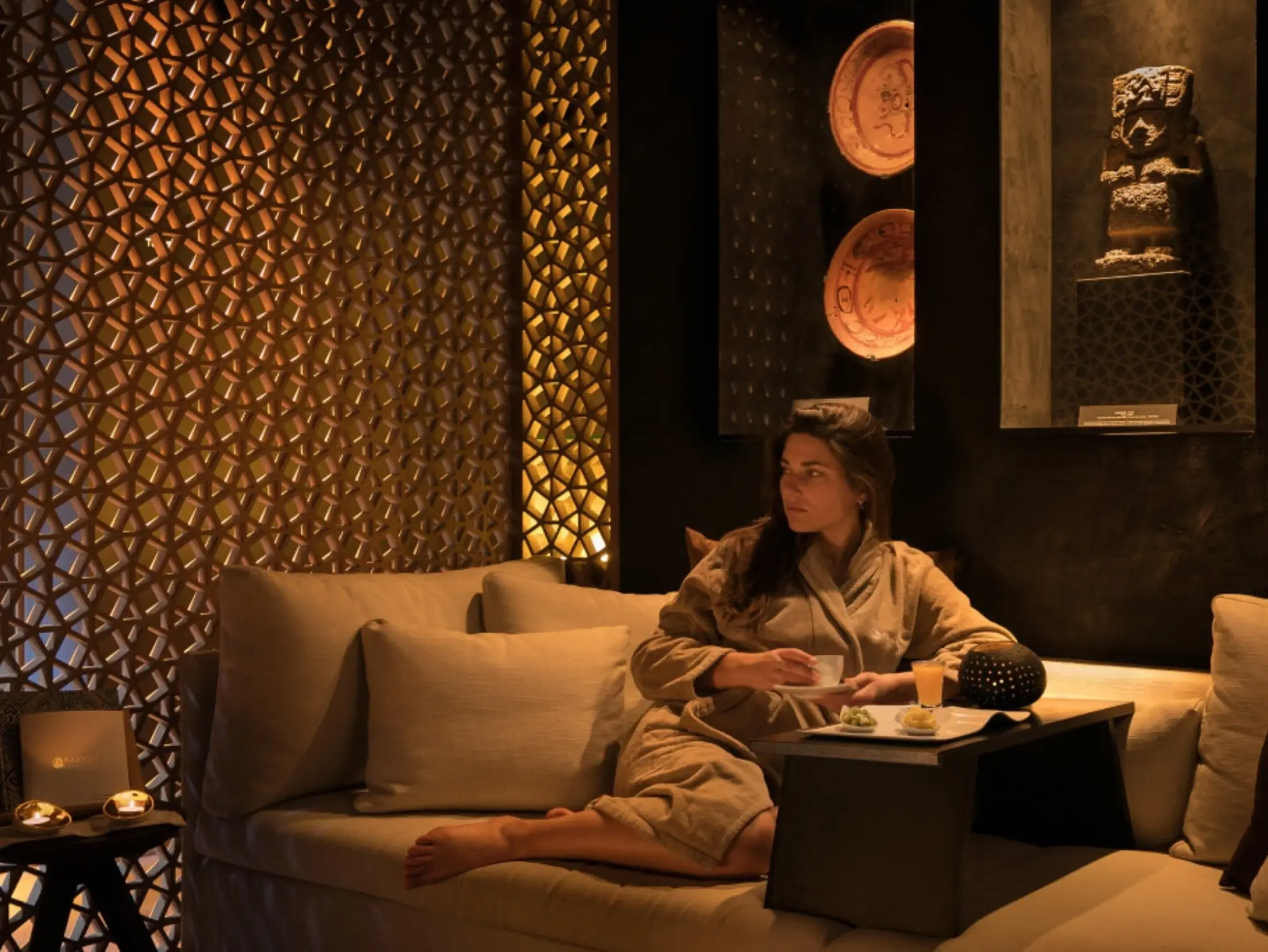 Imagen que muestra un espacio de spa con un ambiente relajante, decorado con tonos cálidos y elementos naturales que evocan la cultura maya.