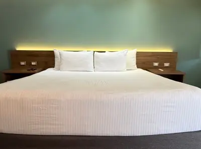 Se ve una cama doble con ropa de cama blanca y dos almohadas sobre una base de madera en un dormitorio.