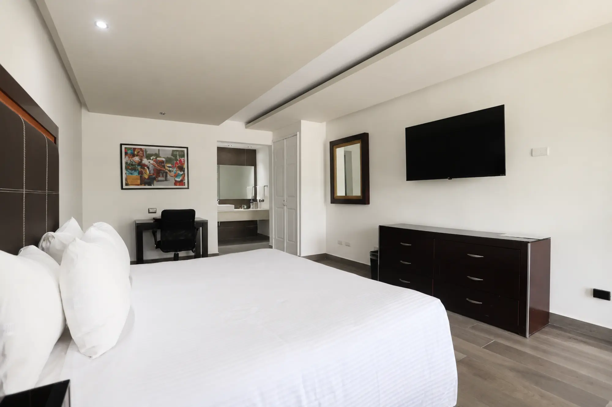 Se ve una cama con ropa de cama blanca, una televisión de pantalla plana y un escritorio en la habitación.