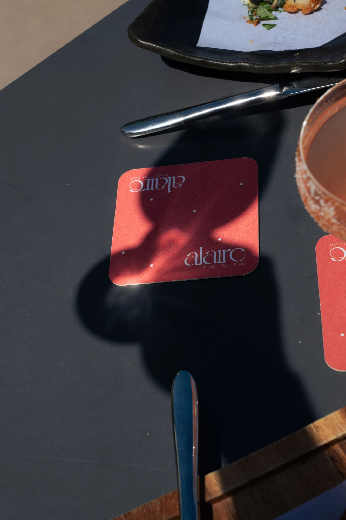 Se ve una tarjeta de menú roja sobre una mesa con cubiertos y un plato al fondo.