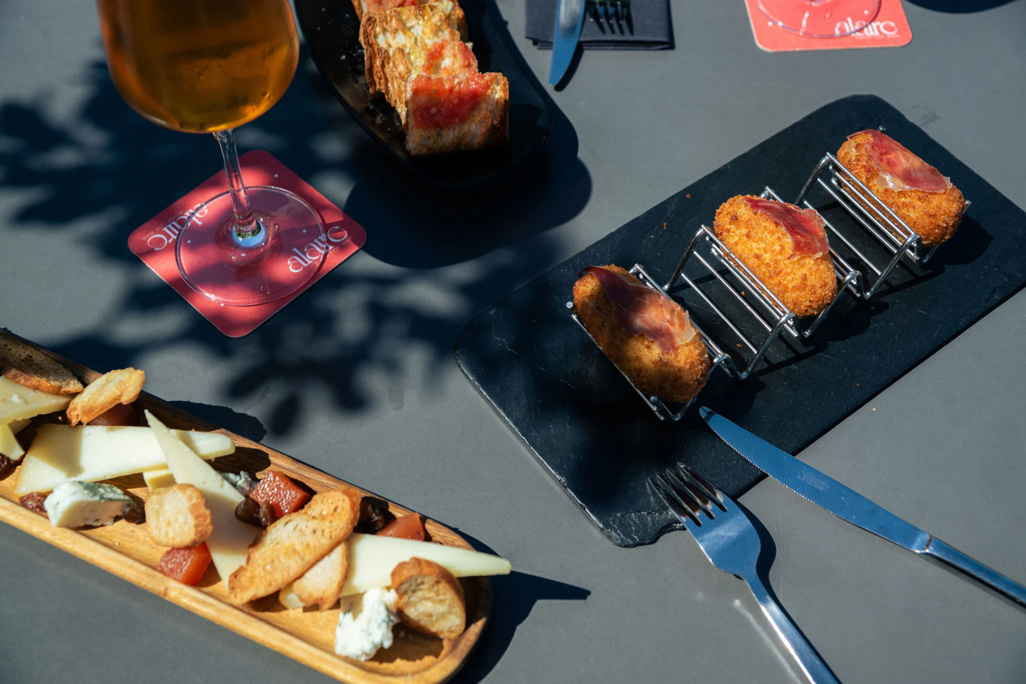 Se ve una mesa con platos de comida, pan y vasos con bebida al aire libre.