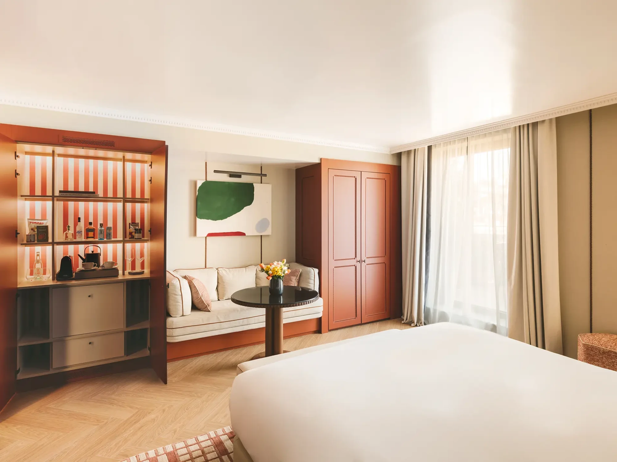 La imagen muestra una cama doble, una mesita con decoración y un armario en una habitación luminosa.